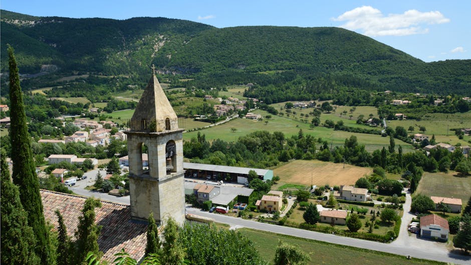 Scenic view of a church tower in a lush valley village surrounded by hills.