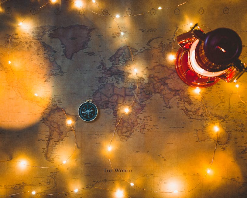 A vintage world map illuminated by string lights with a compass and lantern, evoking travel dreams.