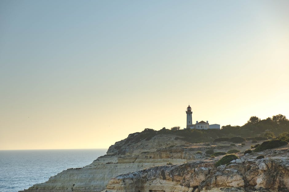 A serene view of a lighthouse on the Algarve cliffs during sunset, Portugal.