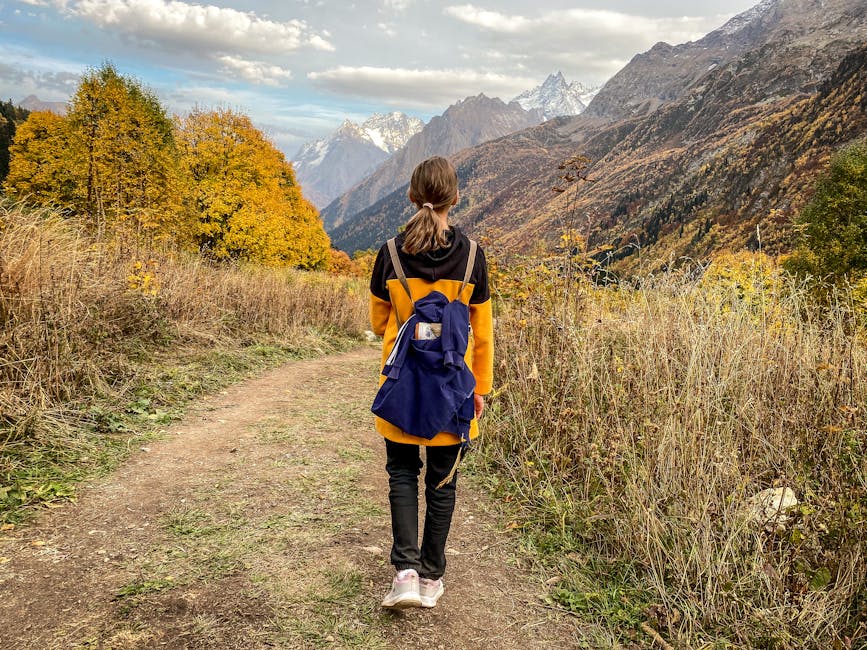 A solitary woman with a backpack hiking through vibrant autumn mountain scenery.